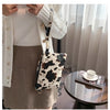 A woman wearing a white sweater and brown skirt holds a leopard print PU leather wrist bag.