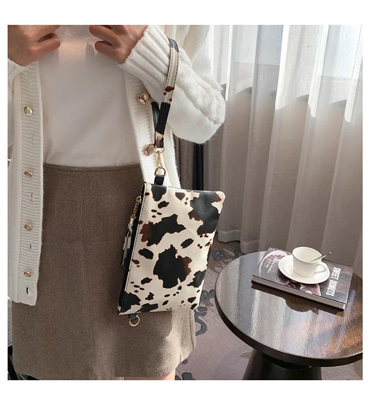 A woman wearing a white sweater and brown skirt holds a leopard print PU leather wrist bag.