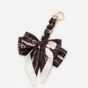 A black fabric bag strap tied in a bow with gold chain detailing and white accents.