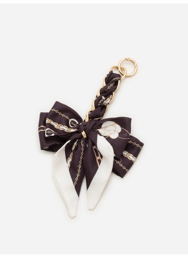 A black fabric bag strap tied in a bow with gold chain detailing and white accents.