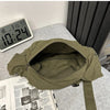 A olive green cotton canvas shoulder crossbody bag lying on a gray surface next to a digital clock and some papers.