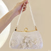 A hand holds a white embroidered pearl chain clutch bag with gold accents.