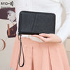 A black RFID blocking travel wallet is shown being held by a person, with a light pink skirt visible in the background.