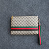 Beige und grün gemusterte Gucci-Clutch mit schwarzem Riemen auf grauem Stoff