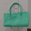A mint green crocodile embossed leather tote bag with a handle and magnetic closure displayed against a white wooden backgrou
