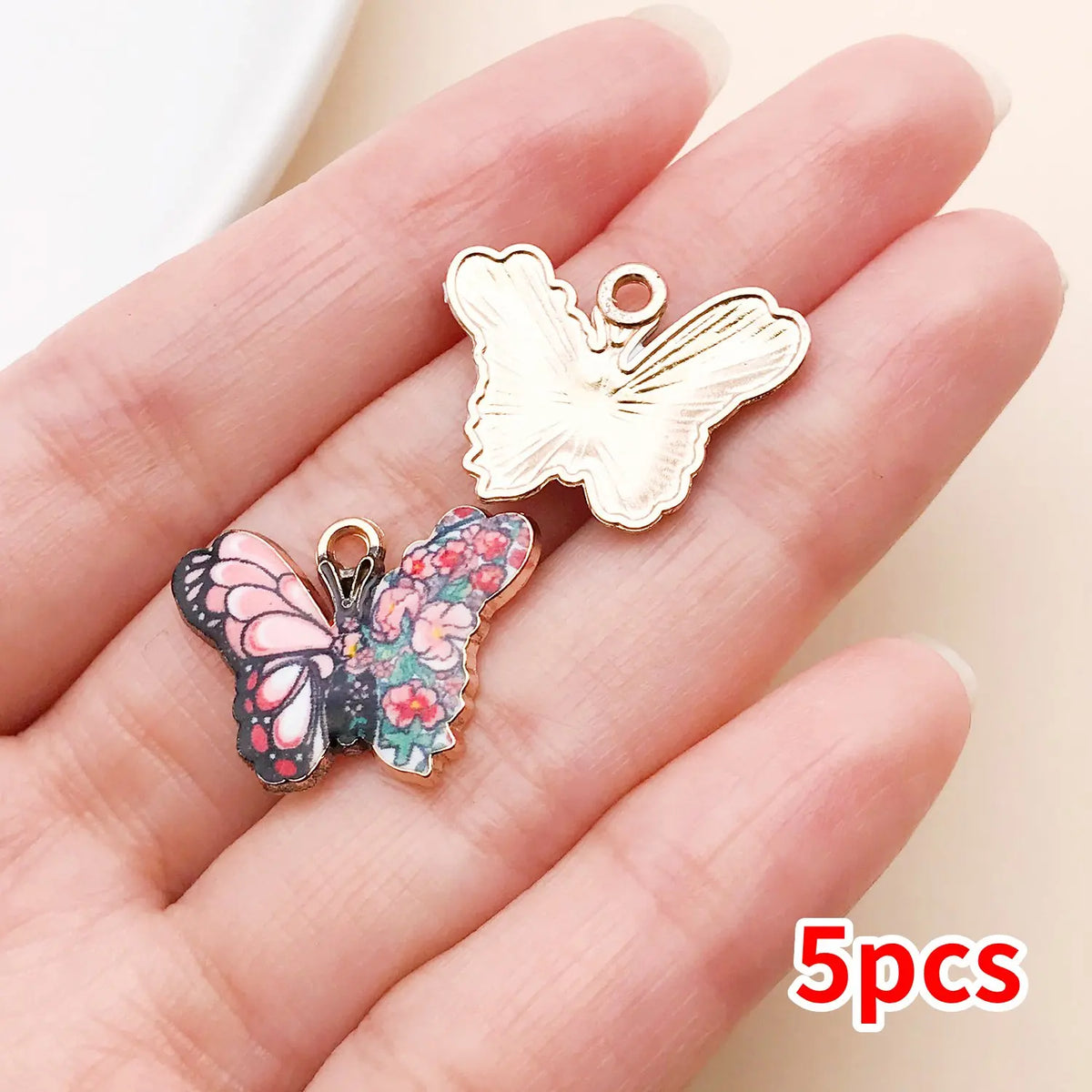 A set of five colorful butterfly enamel charms displayed on a person's hand.