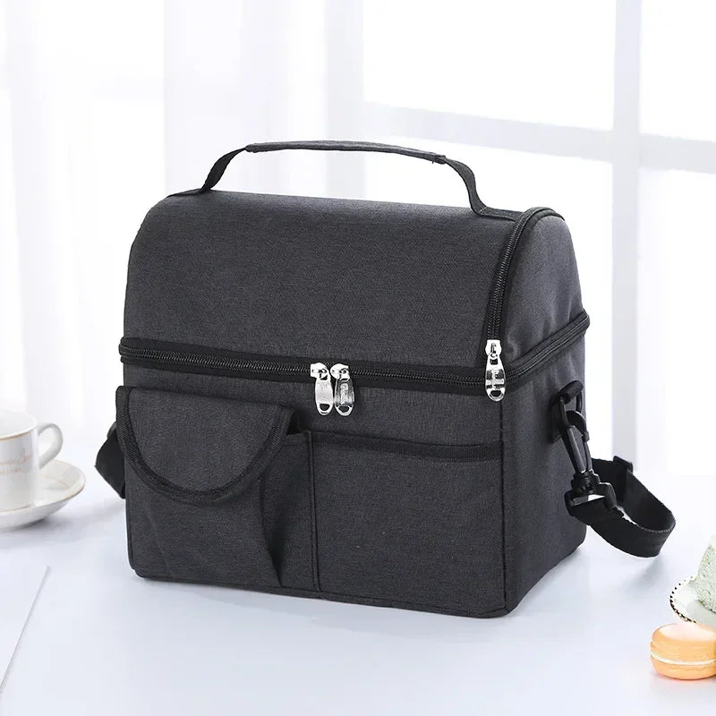 A black reusable insulated lunch bag with a handle and zippered compartments is shown on a white surface.