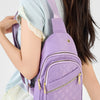 Un sac bandoulière matelassé violet avec une sangle rose porté par une personne dans un haut bleu clair.