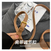 A close-up of a tan PU leather crossbody handbag strap and buckle against a gray fabric background.
