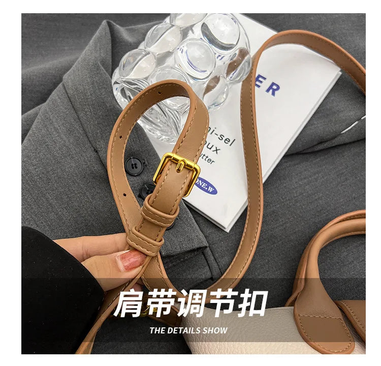 A close-up of a tan PU leather crossbody handbag strap and buckle against a gray fabric background.