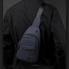 A dark navy nylon crossbody sling bag is shown attached to a black jacket.
