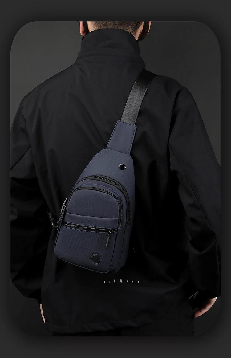 A dark navy nylon crossbody sling bag is shown attached to a black jacket.
