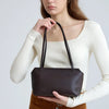 A model wearing a cream long-sleeved top holds a dark brown leather mini shoulder bag.