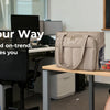A woman is sitting at a desk working while holding food, next to an Insulated Multi-Pocket Work Tote.