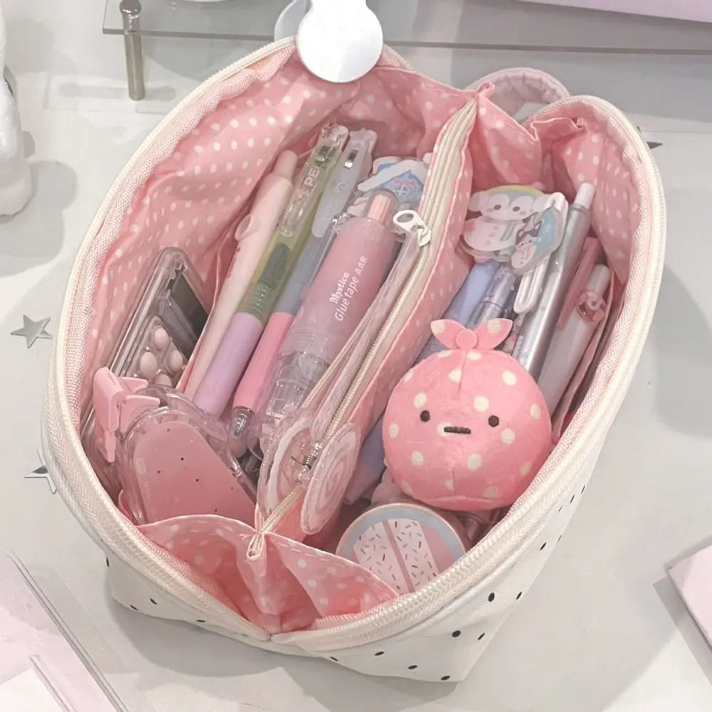 A pink polka dot shell pencil case filled with various pens, pencils, and small accessories.