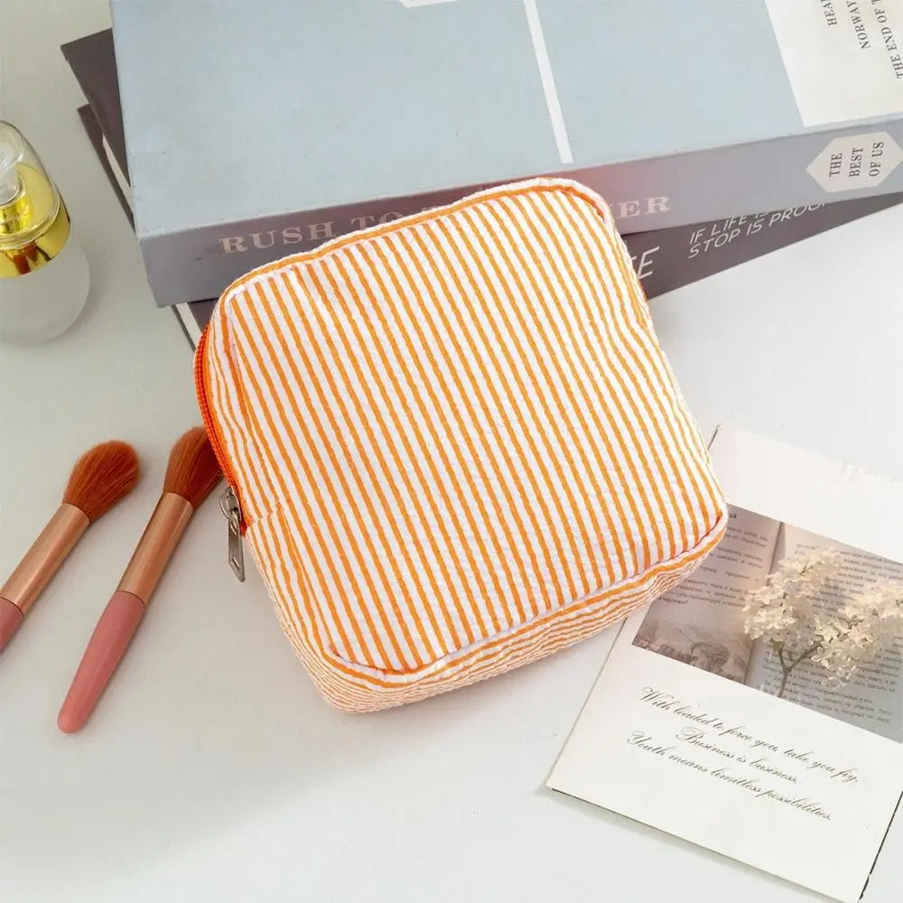An orange and white striped multi-functional storage pouch resting on a white surface next to makeup brushes and books.