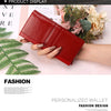 A red genuine leather clutch wallet displayed next to green fern leaves and floral arrangements.