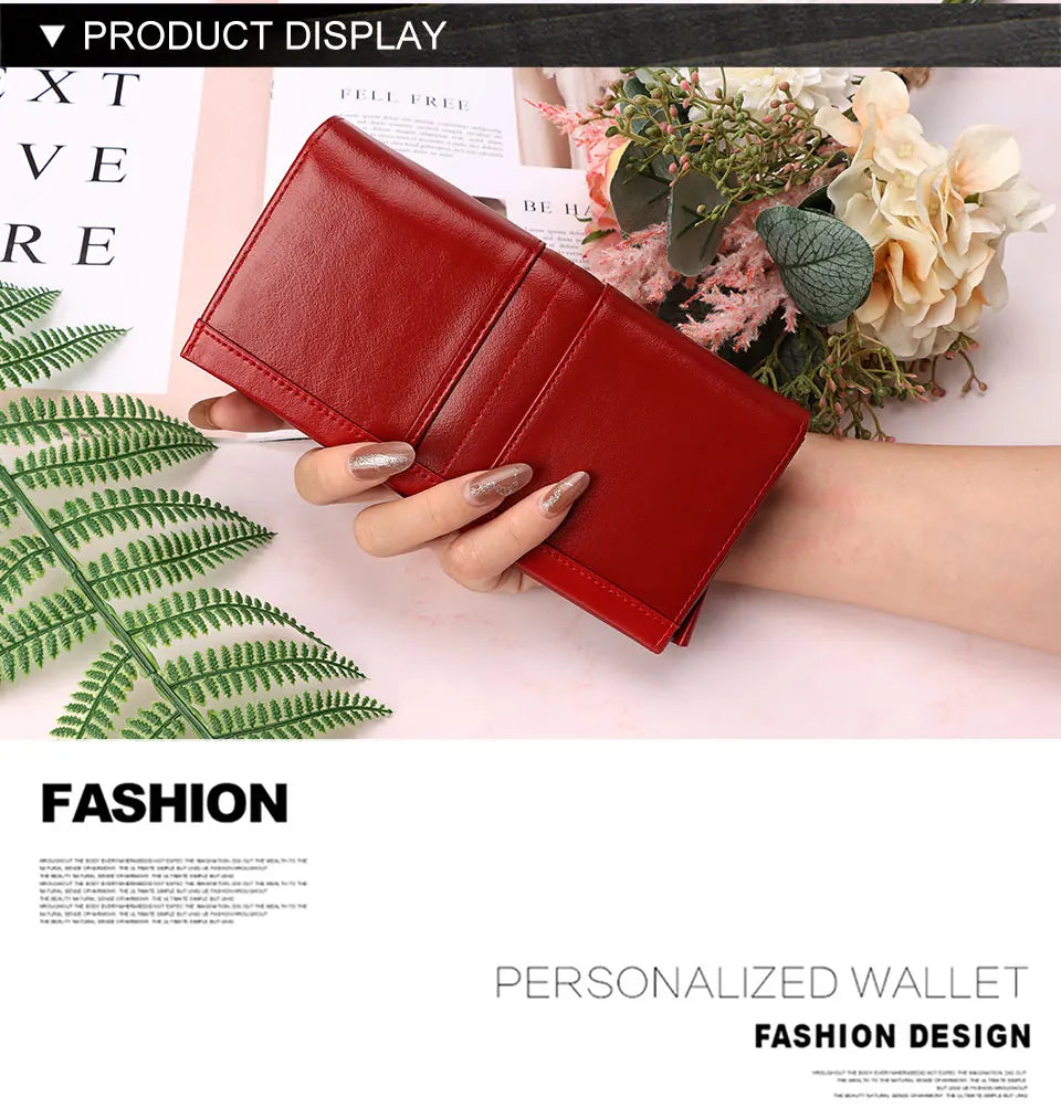 A red genuine leather clutch wallet displayed next to green fern leaves and floral arrangements.
