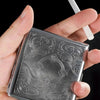 A hand holds a decorative metal cigarette storage box with intricate embossed scrollwork.