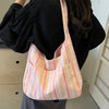 A light striped canvas shoulder bag with a vertical pattern is shown against a dark top.