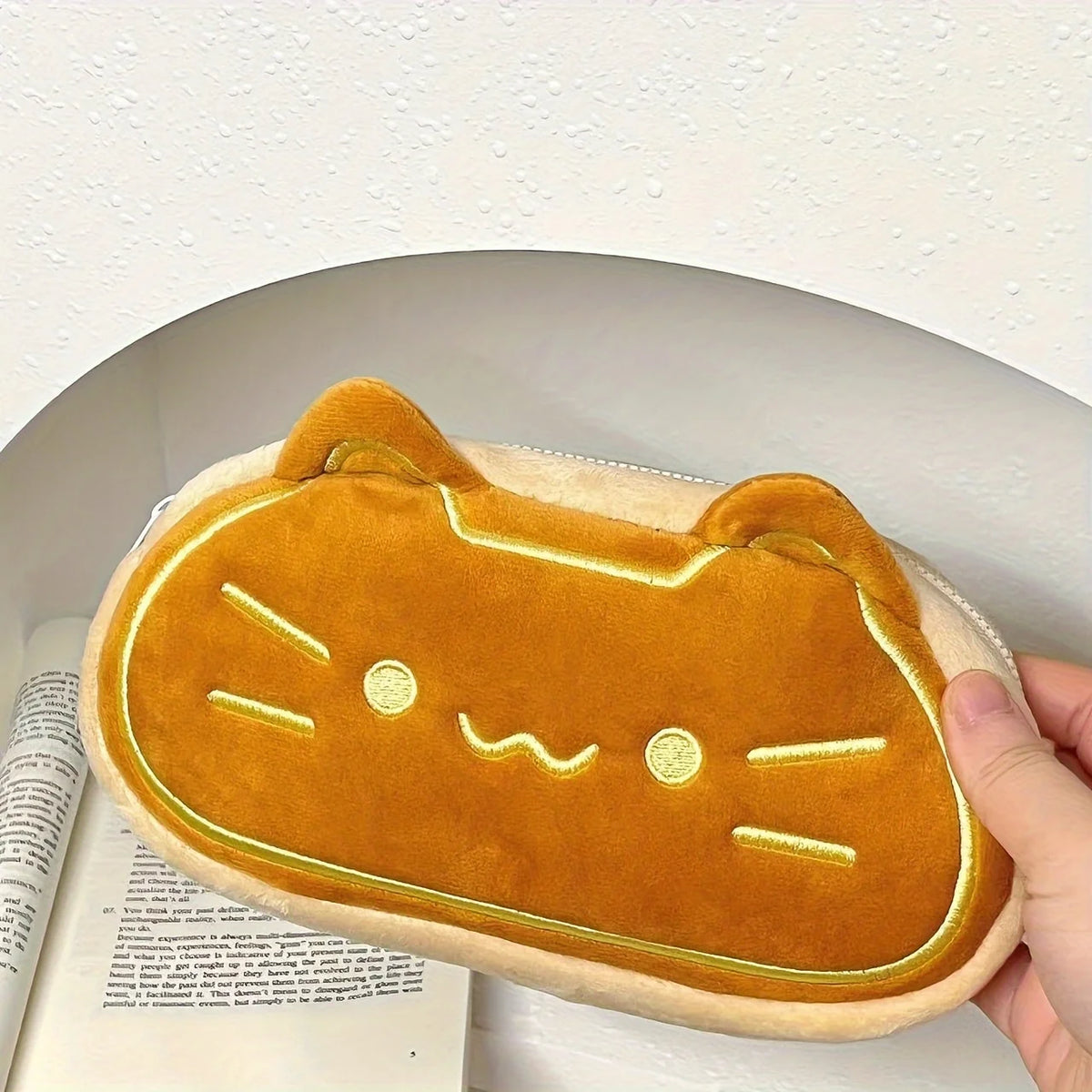 A golden orange cat plush pencil pouch resting on a white surface.