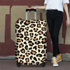 A person is holding a leopard print protective luggage cover for travel bags against a reddish-brown wall.