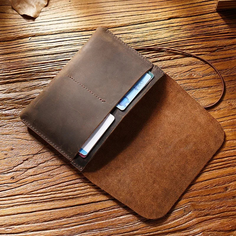 A brown full-grain leather passport holder and card wallet with a blue ID card resting on a wooden surface.