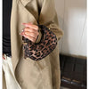 A hand holding a leopard print PU leather mini tote handbag against a beige coat.