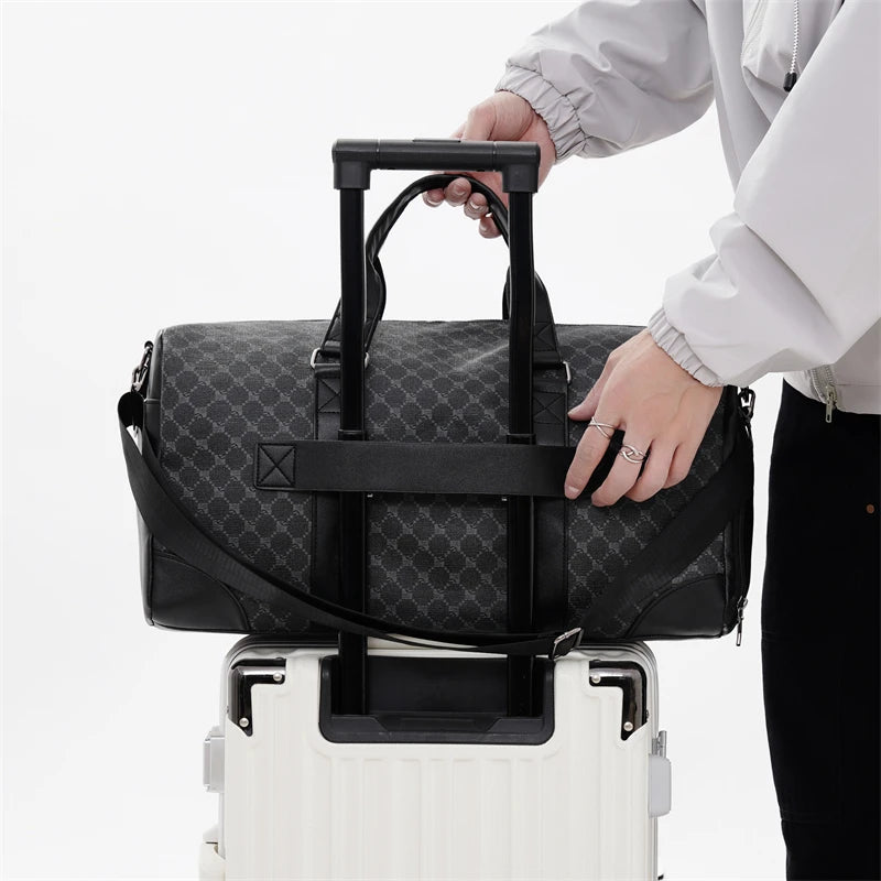 A person is holding a black leather-trimmed travel duffle bag with black handles, resting it on a white rolling suitcase.