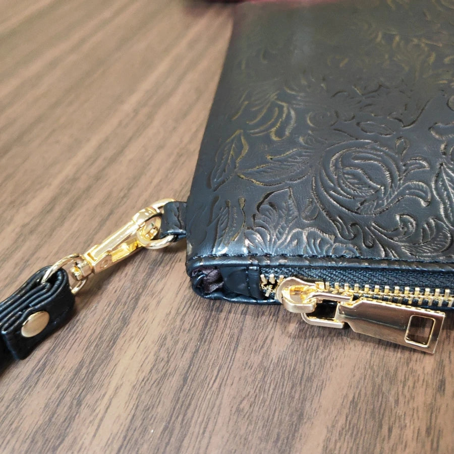 Clutch de cuero PU con estampado floral oscuro y correa y cierre dorado sobre una superficie de madera.