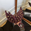A dark purple faux suede hobo crossbody bag with gold rivet accents being held by a hand.