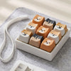 A collection of cute cat-shaped fidget toys and bag charms in various pastel and earthy tones arranged in a white dish.