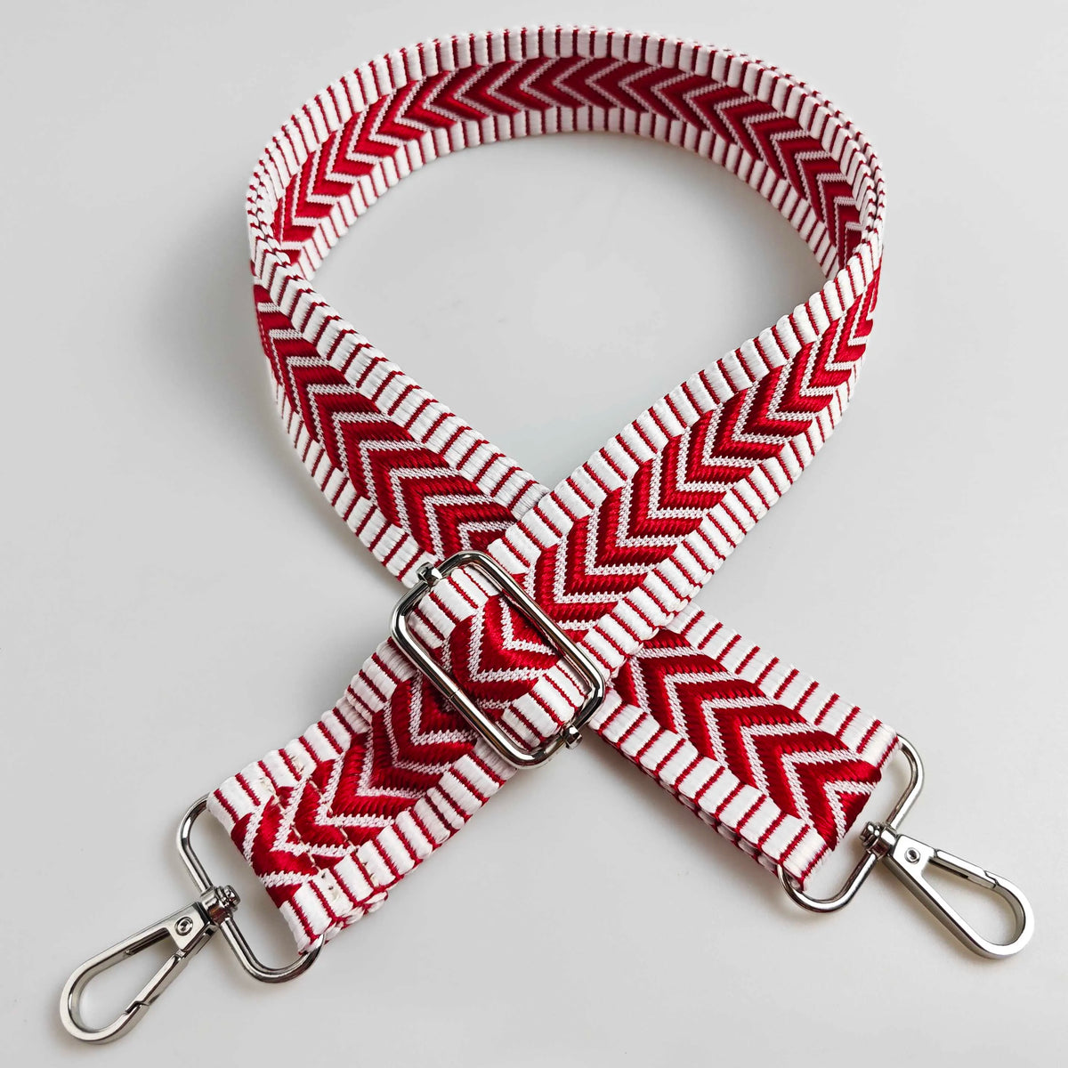 A red and white patterned fabric strap with a silver buckle and metal clasps.
