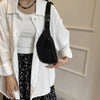 A person wearing a white shirt and jacket holds a black nylon crossbody sling bag.