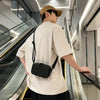 A person wearing a beige t-shirt and hat is standing on an escalator, carrying a black leather shoulder bag.