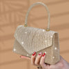 A hand holds a gold glitter sequin crossbody evening bag with a textured fabric.