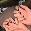 A hand displays a set of cute cartoon press-on nails with various designs on the fingertips.