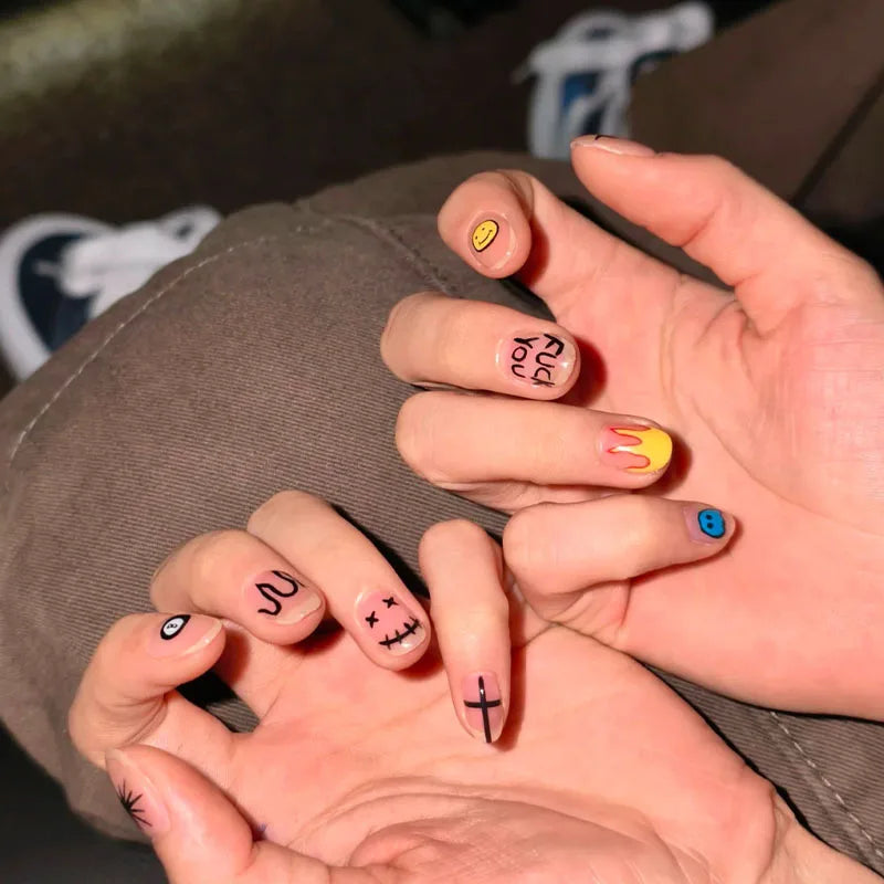 A hand displays a set of cute cartoon press-on nails with various designs on the fingertips.