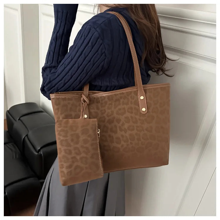 A woman is holding a large brown leopard print tote bag against a white wall.
