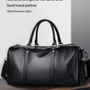 Maleta duffel de cuero negro con asas de cuero sobre una superficie de madera.