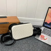 A white quilted shoulder bag with black strap resting on a gray surface next to a laptop.