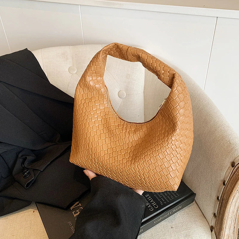 A tan woven embossed hobo shoulder bag with a top handle resting on a black suit jacket.