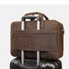 A brown genuine leather briefcase with silver handles resting on top of a black suitcase.