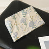 A floral canvas makeup bag featuring blue and green botanical embroidery resting on a black surface.