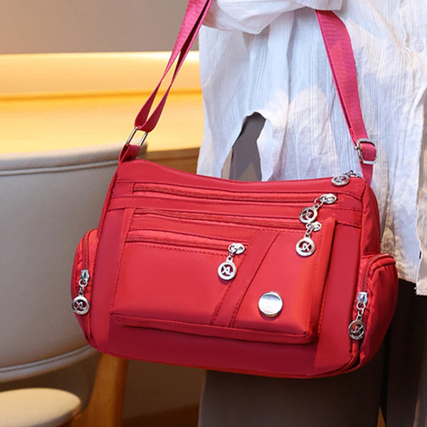 A bright red waterproof nylon crossbody tote bag being held by a person against a light background.