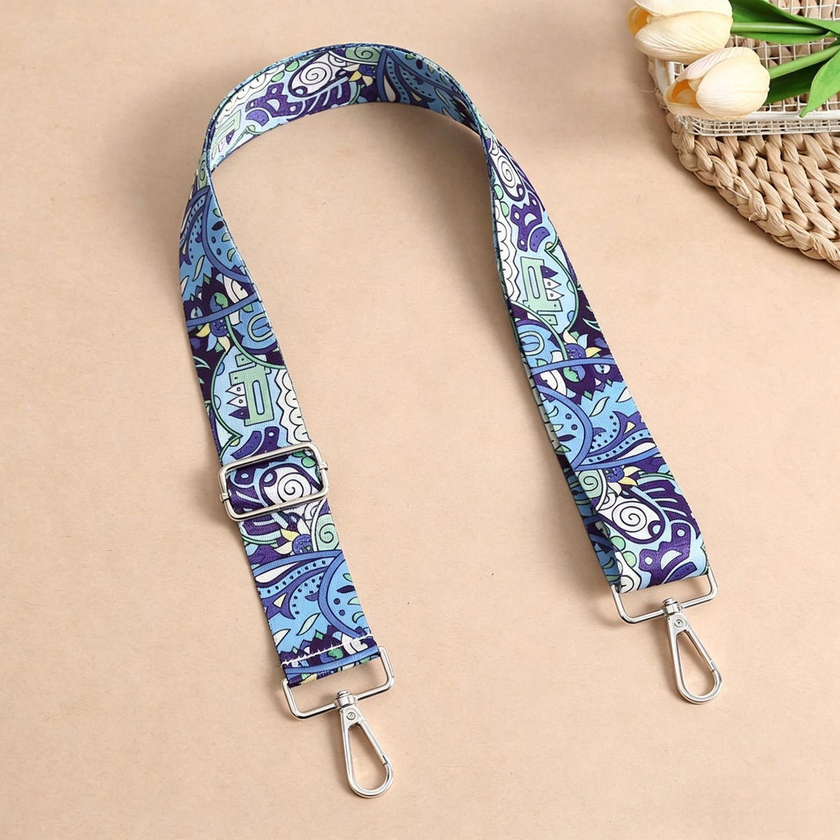 A patterned blue and purple nylon strap with metal buckles is displayed against a beige background.
