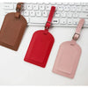 Three PU leather luggage tags in brown, red, and pink colors displayed next to a white computer keyboard.