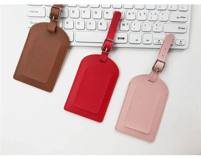 Three PU leather luggage tags in brown, red, and pink colors displayed next to a white computer keyboard.