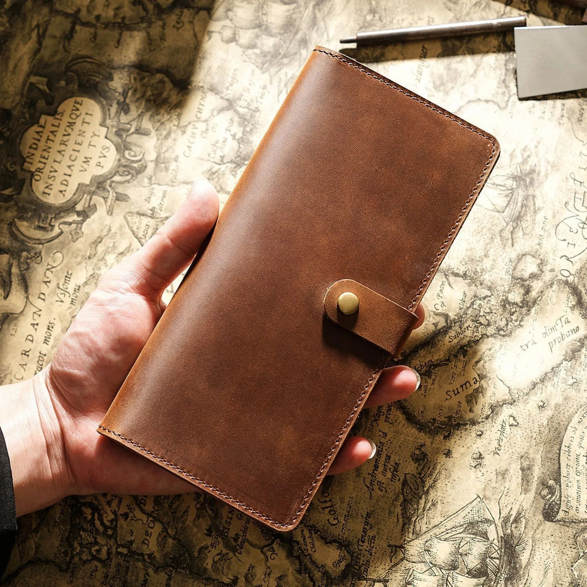 A brown genuine leather long bi-fold wallet with a snap closure is held over an old parchment paper.