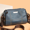 A dark blue leather shoulder bag with gold stitching and a brown strap resting on a light background.